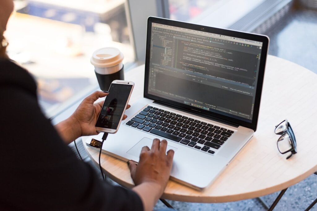 pexels-photo-1181244 Developer working remotely, coding on a laptop with phone in hand, showcasing modern work culture. Kodulehe haldus ja hooldus.